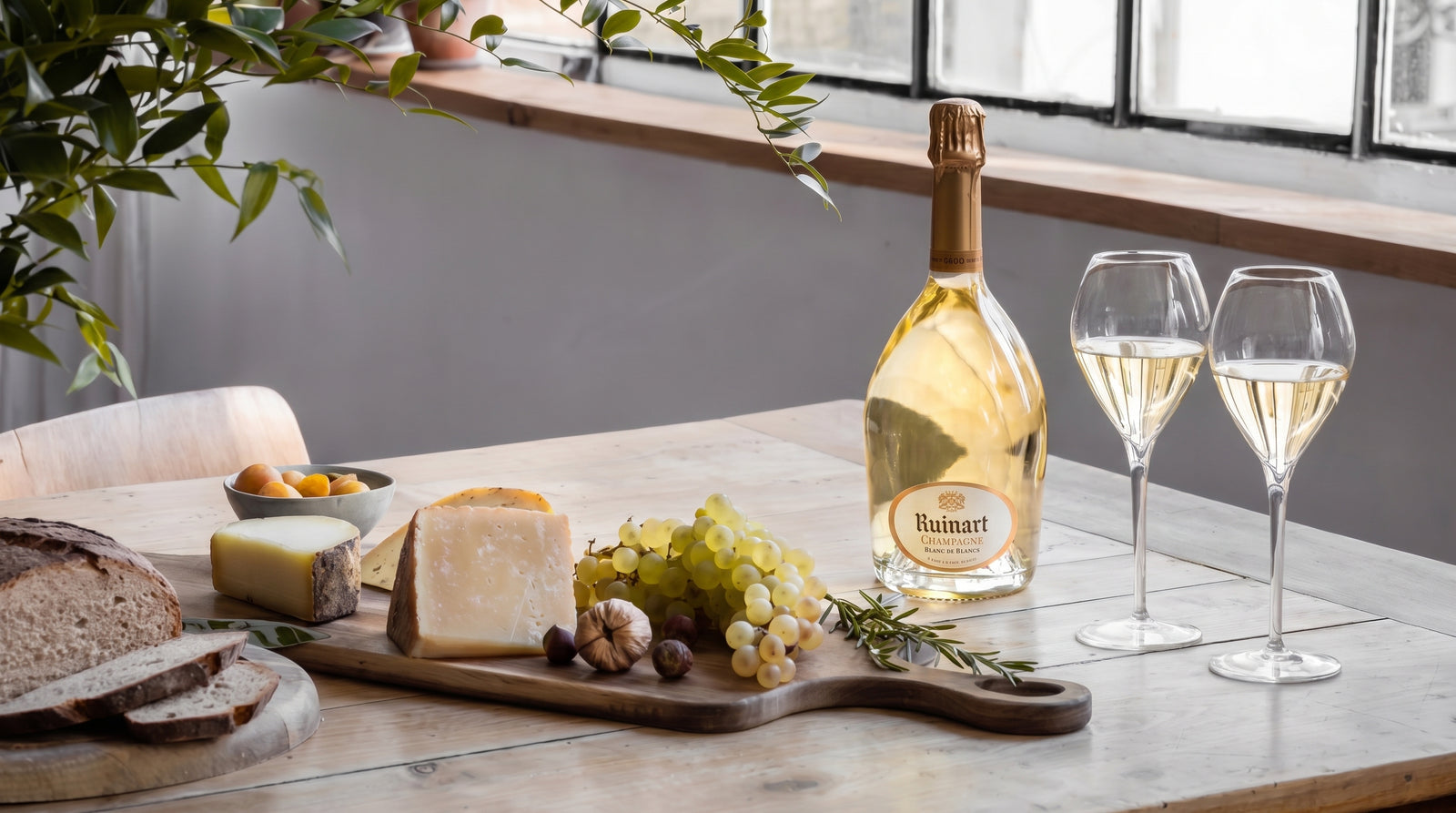 A bottle of Ruinart Blanc de Blancs and two filled glasses on a pale wood table